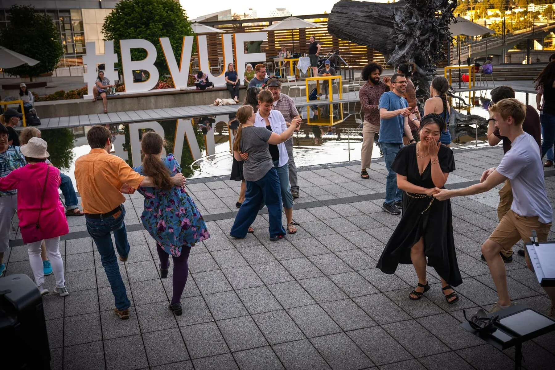 Dancers on the Bellevue City Hall plaza in front of the large Bellevue sign, the reflecting pool behind them, at the 2026 free jazz and swing dance series.