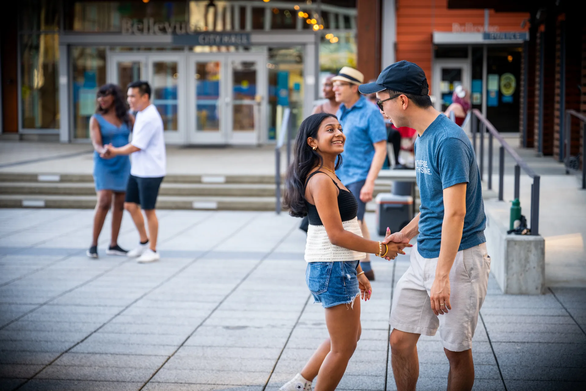 Two dancers smiling at each other mid dance on the Bellevue City Hall plaza, other couples behind them.