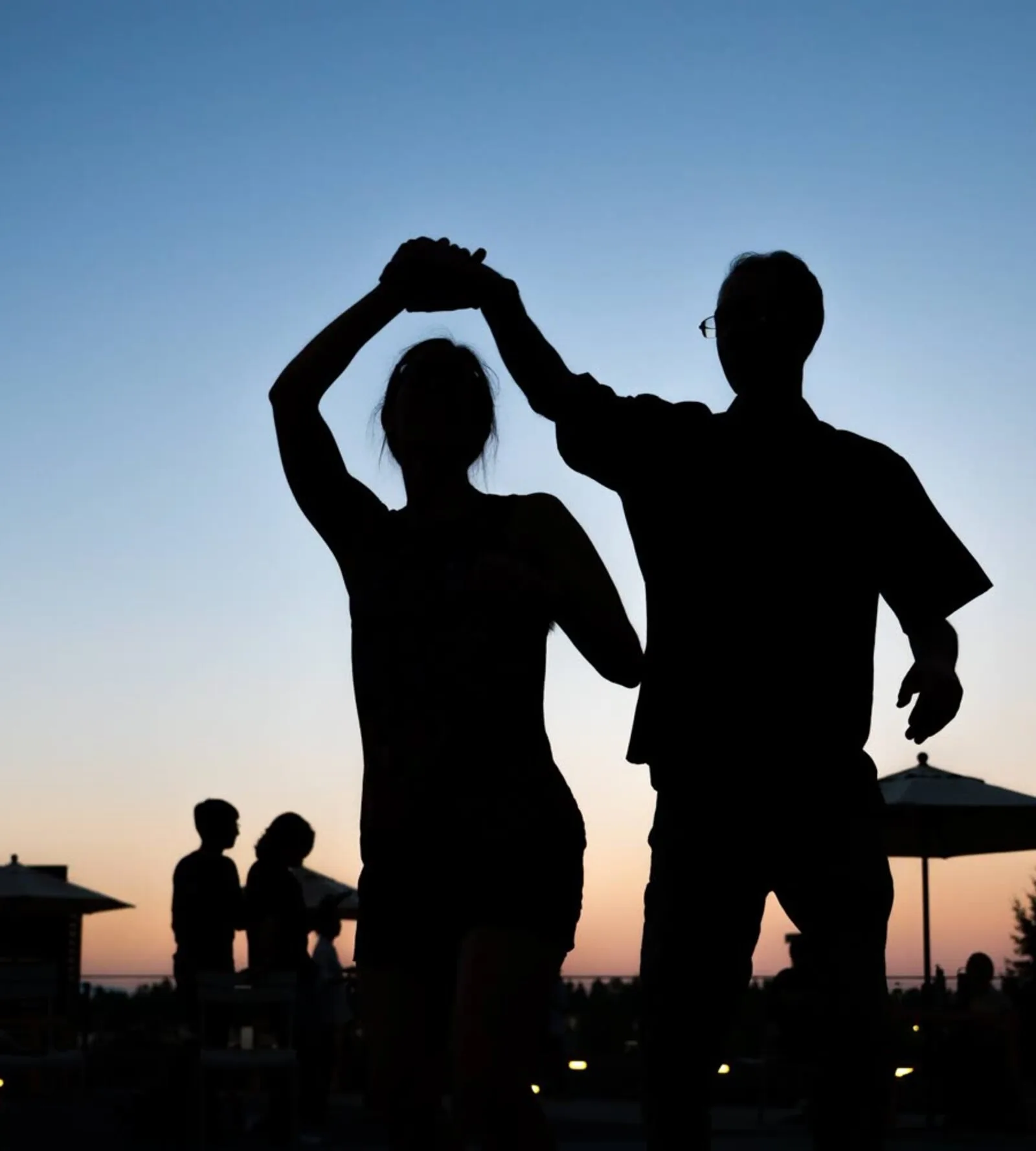 A dancer turning under their partner's raised arm, silhouetted against an evening sky.